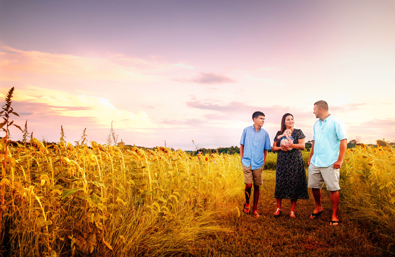 Newborn Photographer, Mom and dad walk through tall dry grassy field with son and baby