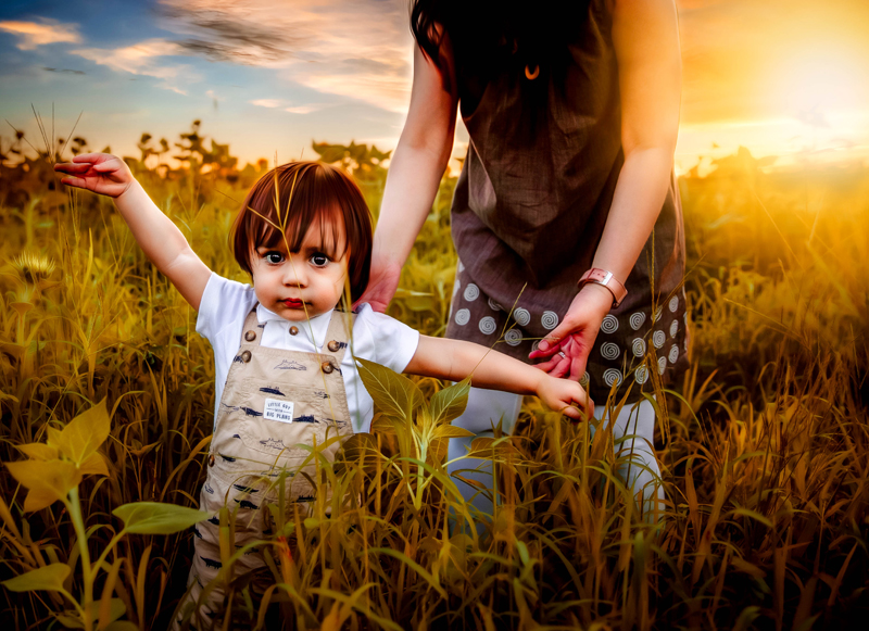Family Photographer, Toddler boy walks through grassy field near his mother